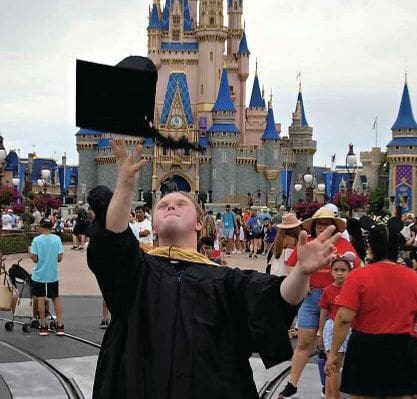 Nicholas McGee throws his graduation cap in the air in front of Cinderella Castle.
