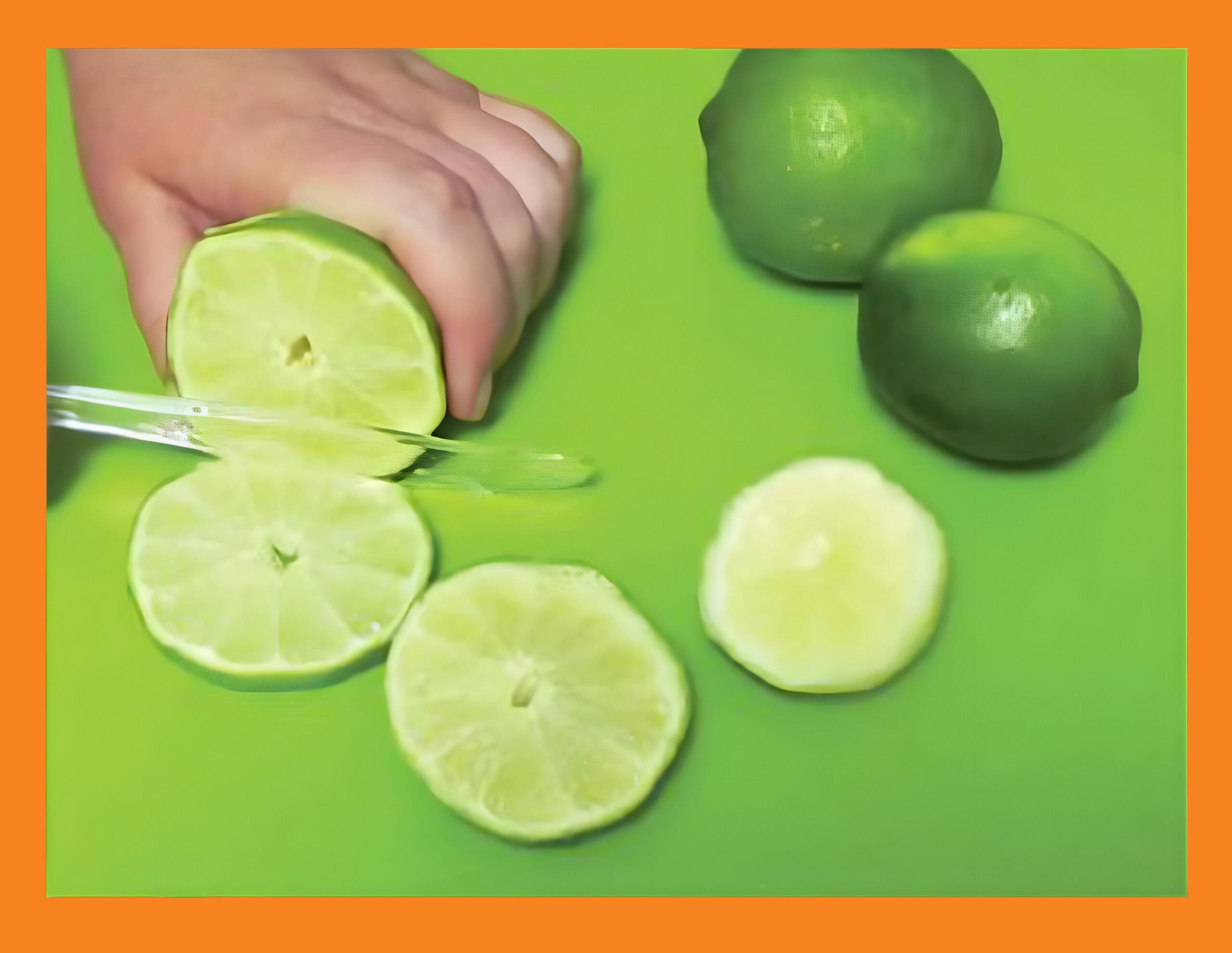 A hand slices a lime on a green cutting board with other limes nearby.