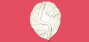 White abstract clay face with circular indentations and a wavy line across the center.