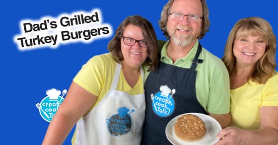 Three people smile at the camera, two wearing aprons, with a grilled turkey burger on a plate.