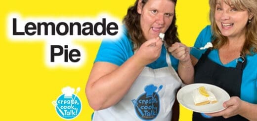 Two women with a lemonade pie, one holds a slice on a plate, the other samples a piece.