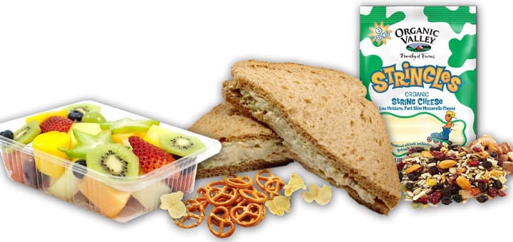 Sandwich, fruit salad, pretzels, trail mix, and string cheese for a healthy meal.