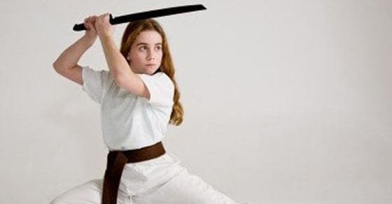 Child in a karate uniform and brown belt holding a practice sword in a martial arts stance.