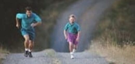 Two people run on a dirt path outdoors.