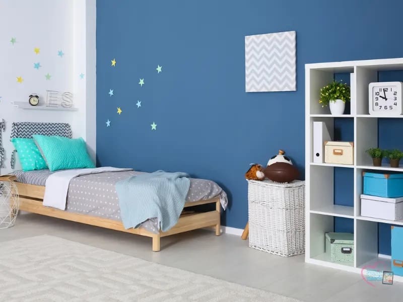 A blue-walled bedroom with a twin bed and a white cube shelf.