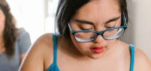 A young person with Down syndrome wearing glasses looks down.