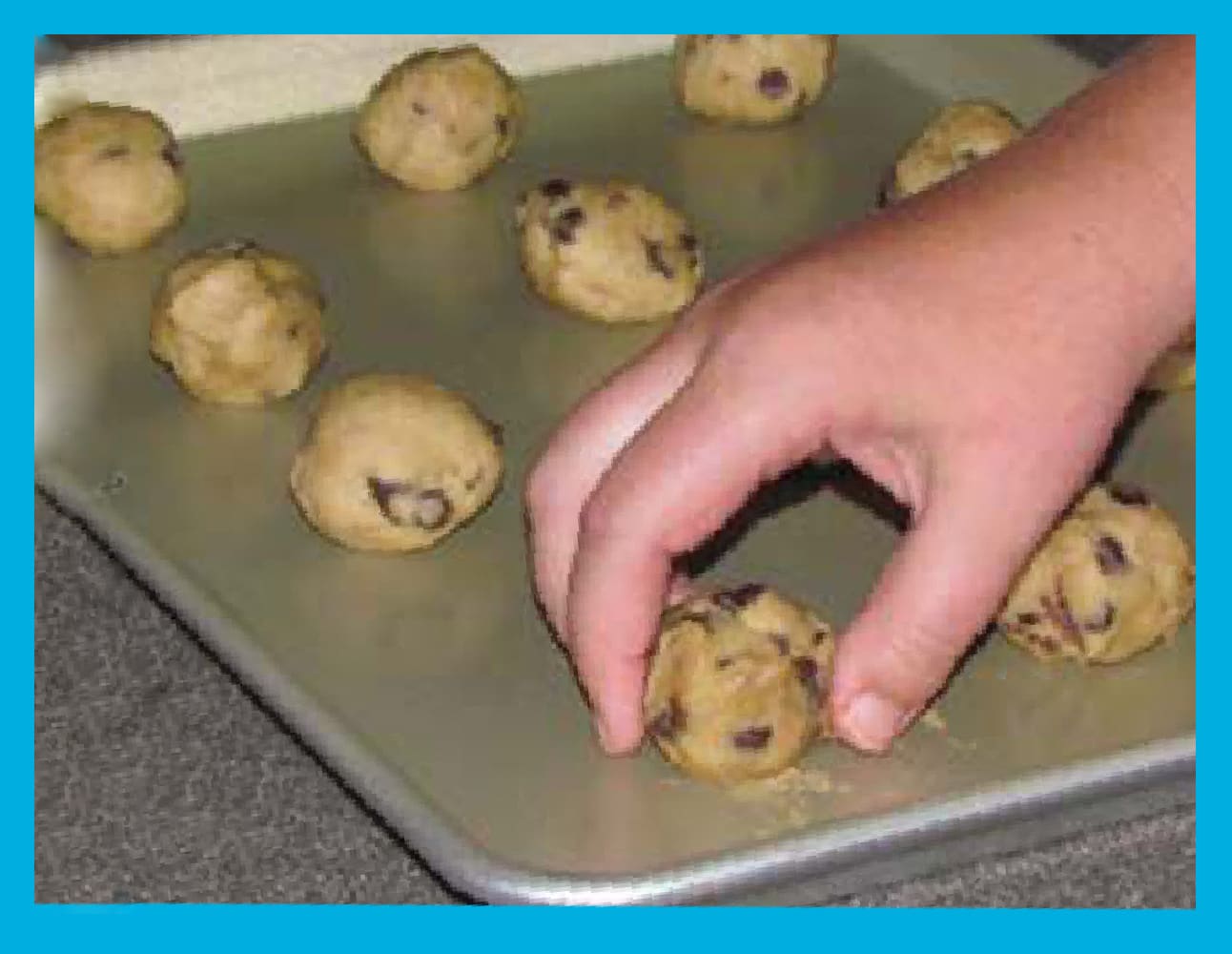 A child's hand places cookie dough balls on a baking sheet.