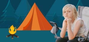 A child sits with their chin resting on their hands in front of a tent and campfire.