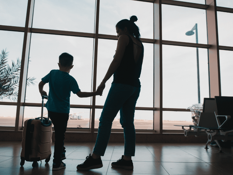 Woman and child holding hands in airport with luggage