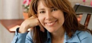 A woman smiles with her head resting on her hand.