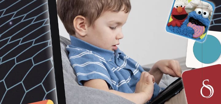Child wearing a blue striped shirt uses a tablet with interactive learning apps featuring Sesame Street characters.