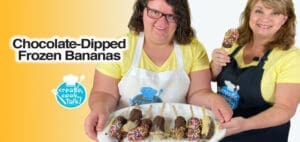 Two women hold a tray of chocolate-dipped frozen bananas.