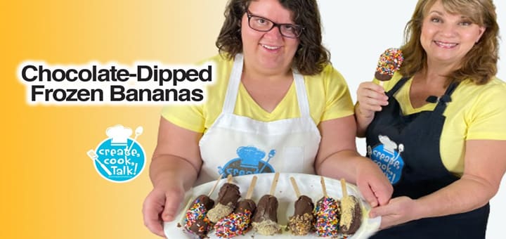 Two women hold a tray of chocolate-dipped frozen bananas.