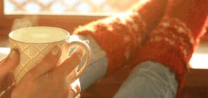 Hands hold a warm mug of tea near a person in fuzzy socks.