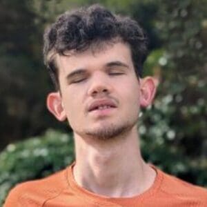 Gabe with eyes closed wearing an orange shirt outdoors