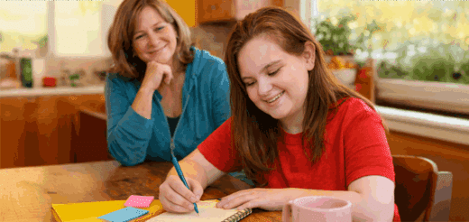Two women smile as one writes in a notebook at a table.