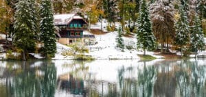 A lodge sits by a calm lake surrounded by snow-dusted trees.