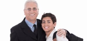 Man in a suit and glasses with his arm around a smiling boy in a collared shirt.