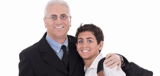 Man in a suit and glasses with his arm around a smiling boy in a collared shirt.