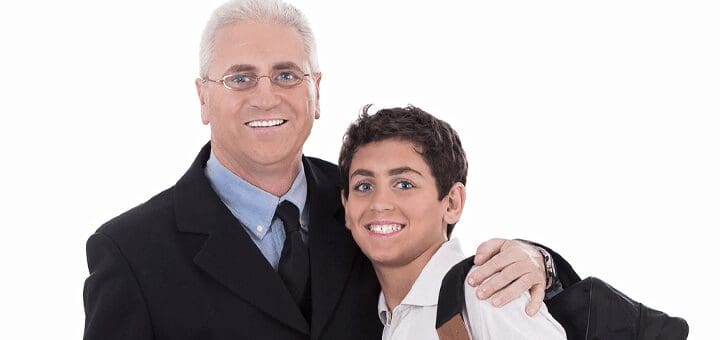 Man in a suit and glasses with his arm around a smiling boy in a collared shirt.