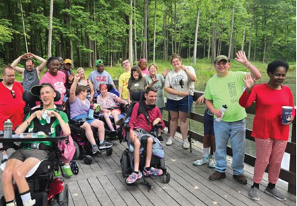 Group of people in wheelchairs and standing on a wooden pier by a lake.