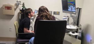 Two children watch a TV screen in a medical room next to an oxygen tank.