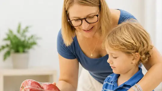 Woman in glasses teaching young boy about meat in a kitchen setting.
