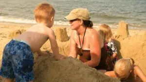 A woman and three children build sandcastles on a beach.