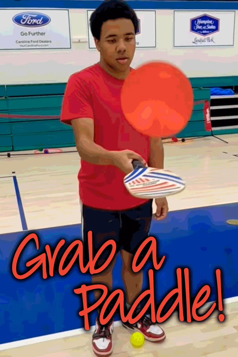 A young person in a red shirt holds a paddle and a ball.