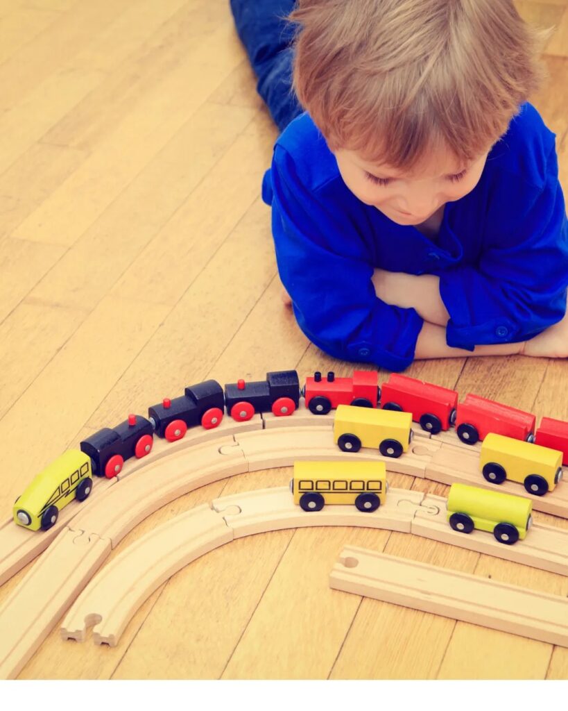 Young child looking down at a wooden interlocking toy structure on the floor.